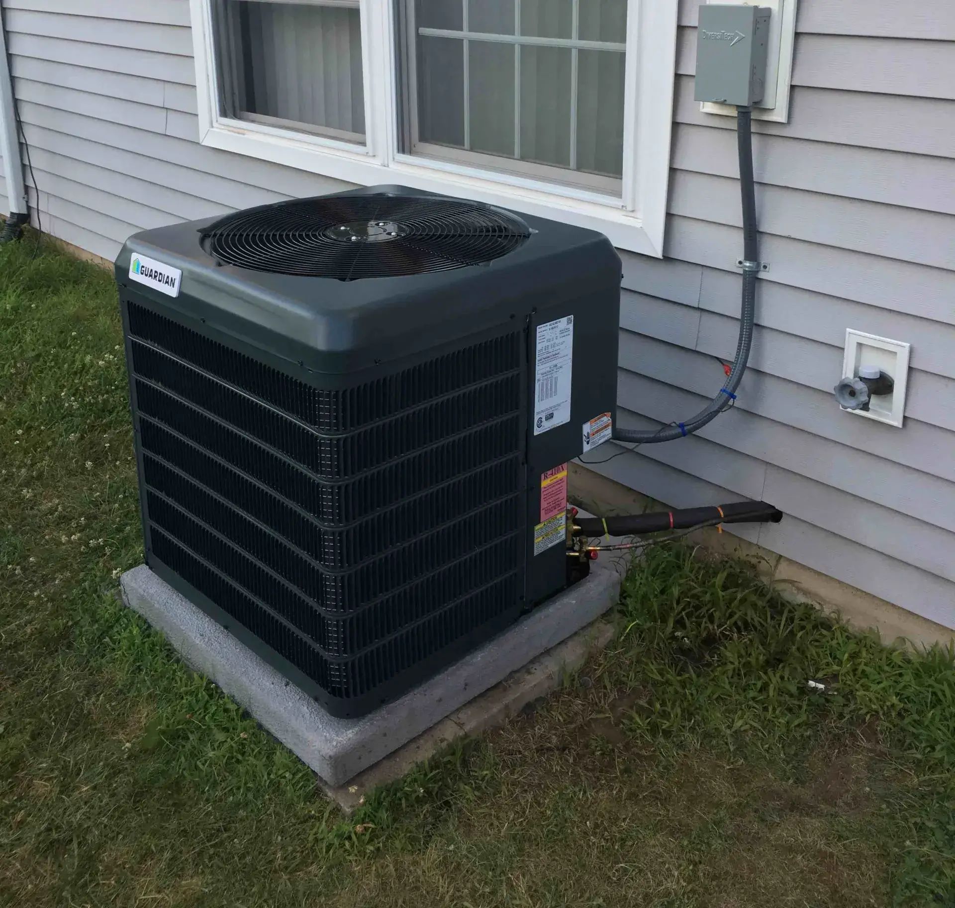 New central air conditioning condenser installed on a concrete pad beside a house