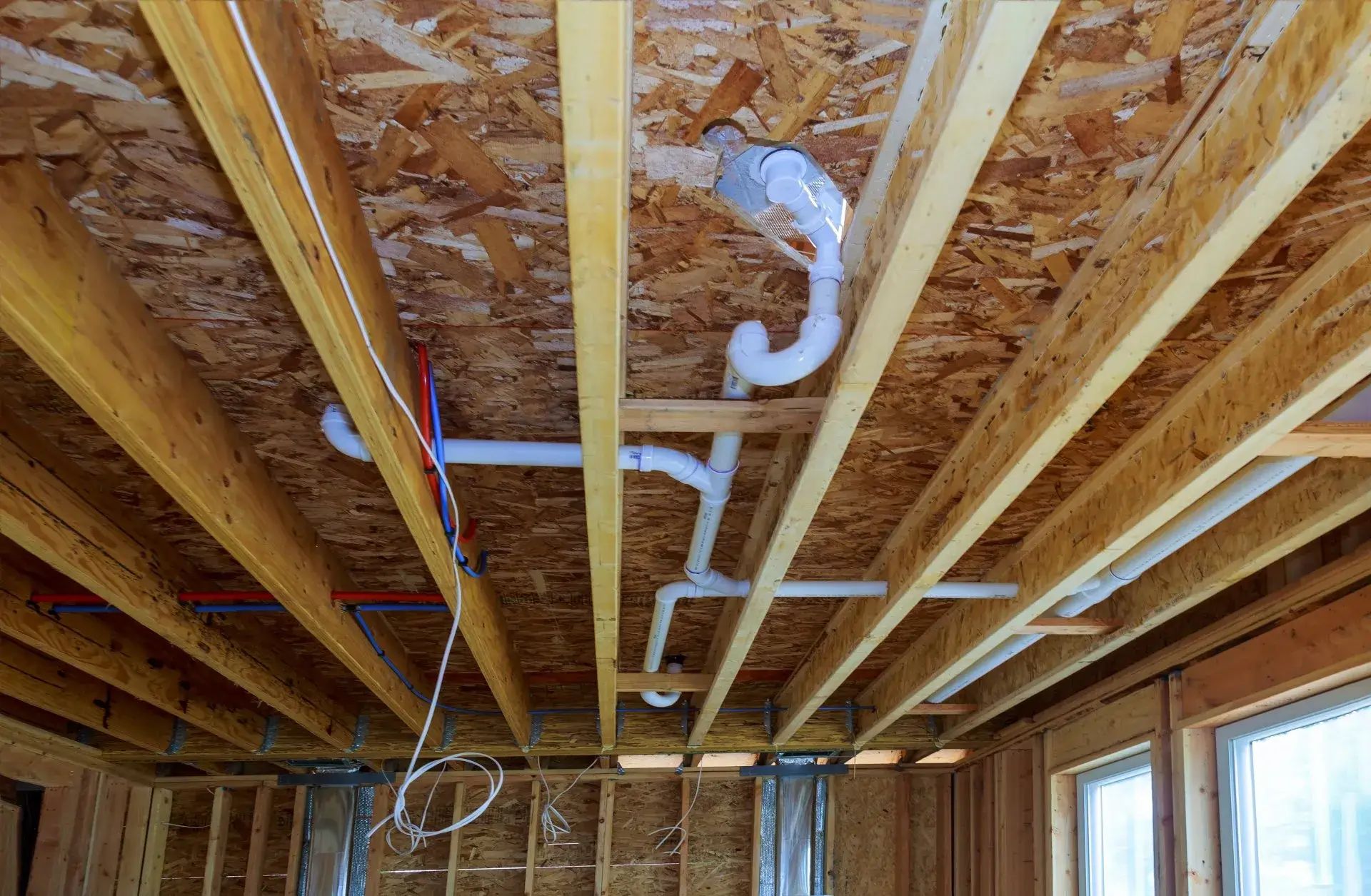 New white PVC drain and vent lines run through open floor joists